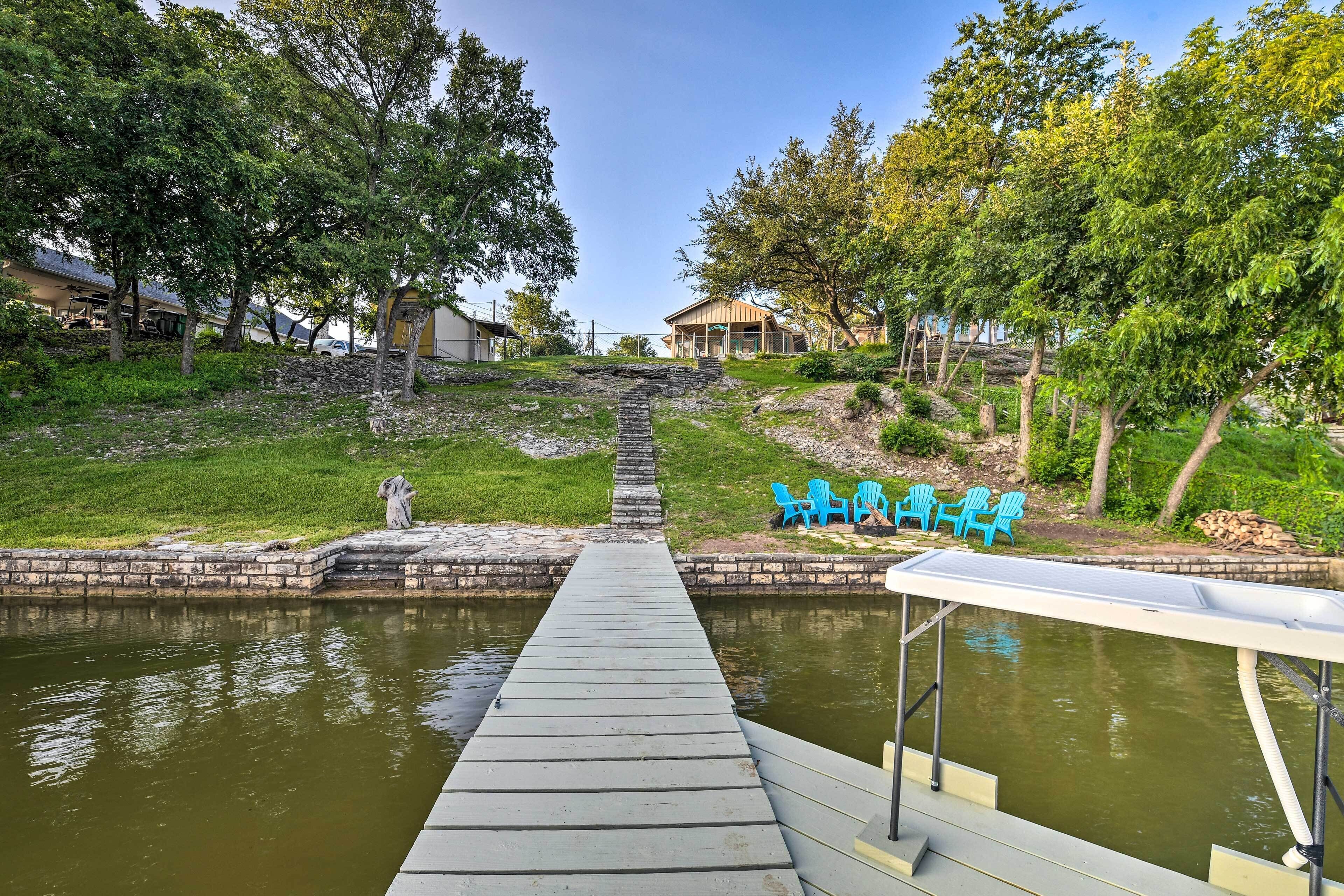 A concrete dock leading into a body of water, surrounded by greenery and a stone pathway.