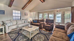 A living room with a high ceiling, wooden beams, a ceiling fan, and a view of the outside.