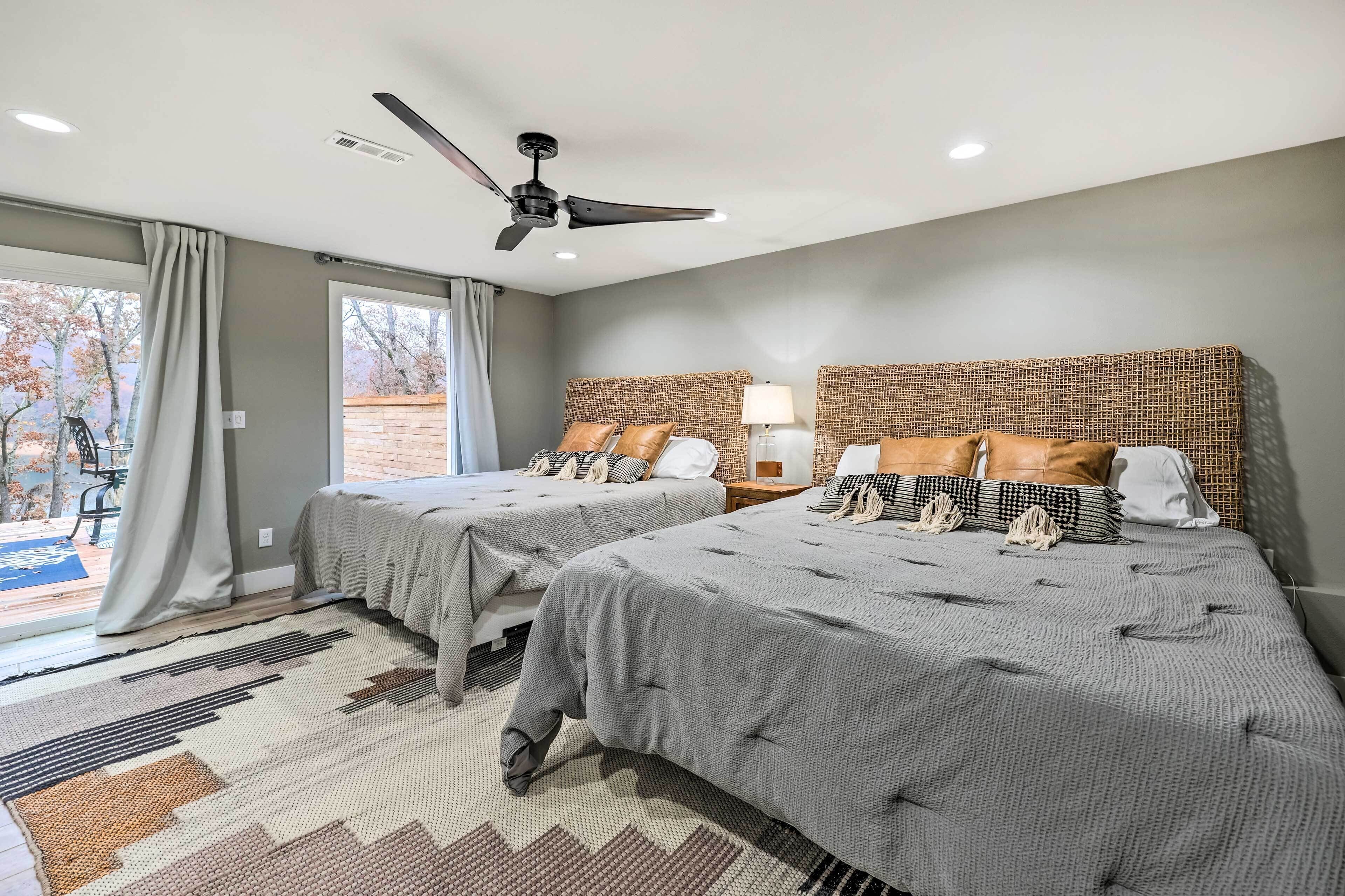 A hotel room with two beds, a ceiling fan, a large window with curtains, and a patterned rug.