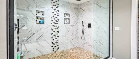 A modern bathroom with a glass-enclosed shower, marble tiles, and a pebble-patterned floor.