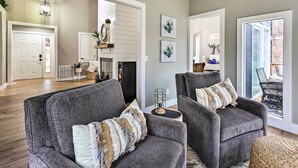 Un salon avec deux fauteuils gris, une cheminée et une vue sur l’extérieur.