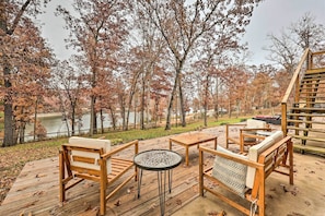 A wooden deck with outdoor furniture overlooking a lake, surrounded by trees with autumn foliage.