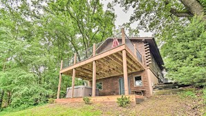 A rustic cabin with a wooden deck and a covered porch, surrounded by dense trees. - Cozy Amish Country Cabin on Shipshewana Lake! (Shipshewana)