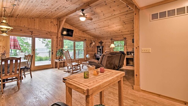 A wooden cabin interior with a dining area, a living room with a sofa and a fireplace, and a ceiling fan. - Cozy Amish Country Cabin on Shipshewana Lake! (Shipshewana)