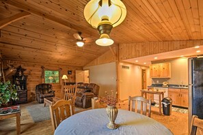 A cozy cabin interior with a dining area, a leather sofa, a ceiling fan, and a kitchen with wooden cabinets. - Cozy Amish Country Cabin on Shipshewana Lake! (Shipshewana)