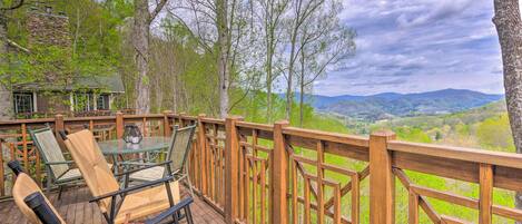A wooden deck with outdoor furniture, a stone building, and a view of green hills.