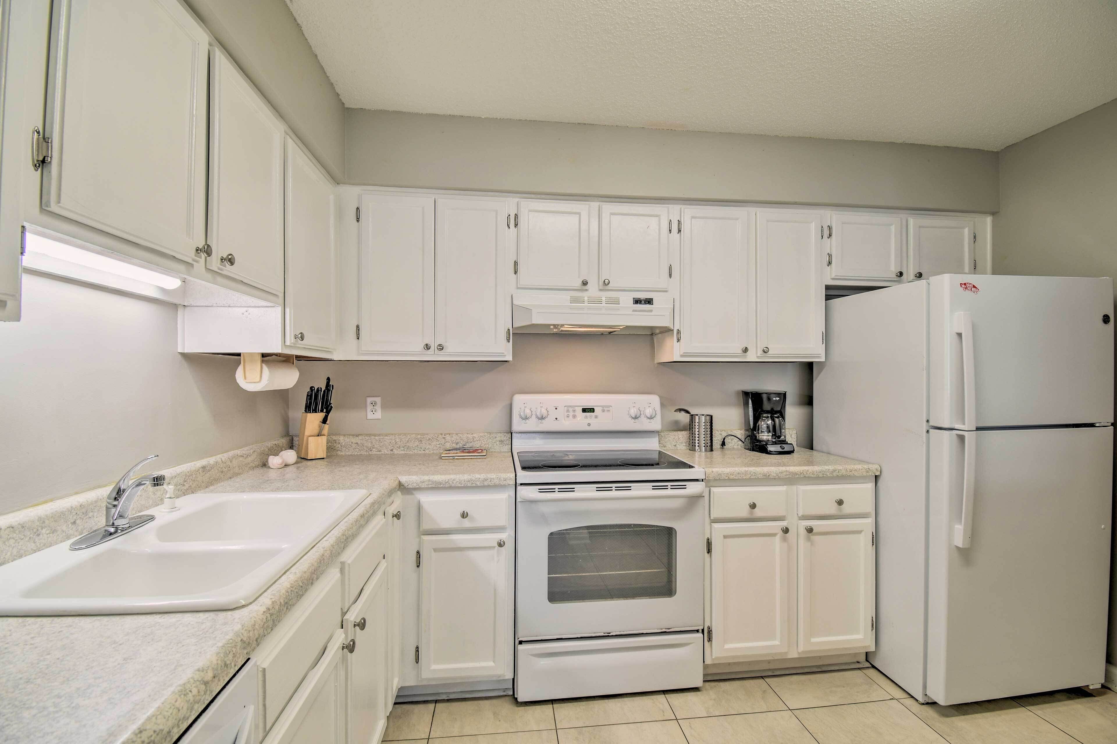 A kitchen with white cabinets, a sink, a stove, and a refrigerator.