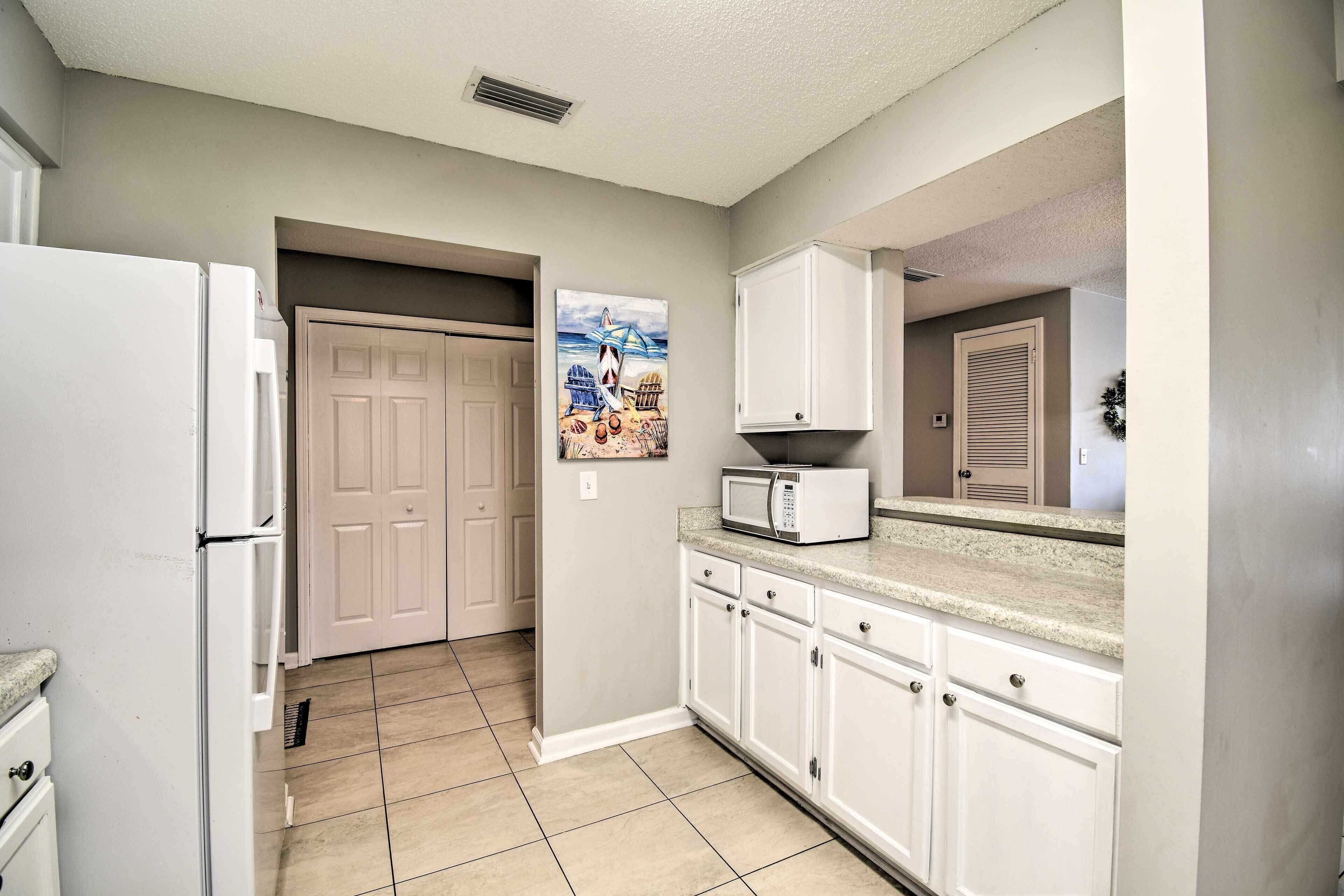A kitchen with white cabinets, a microwave, and a door leading to another room.