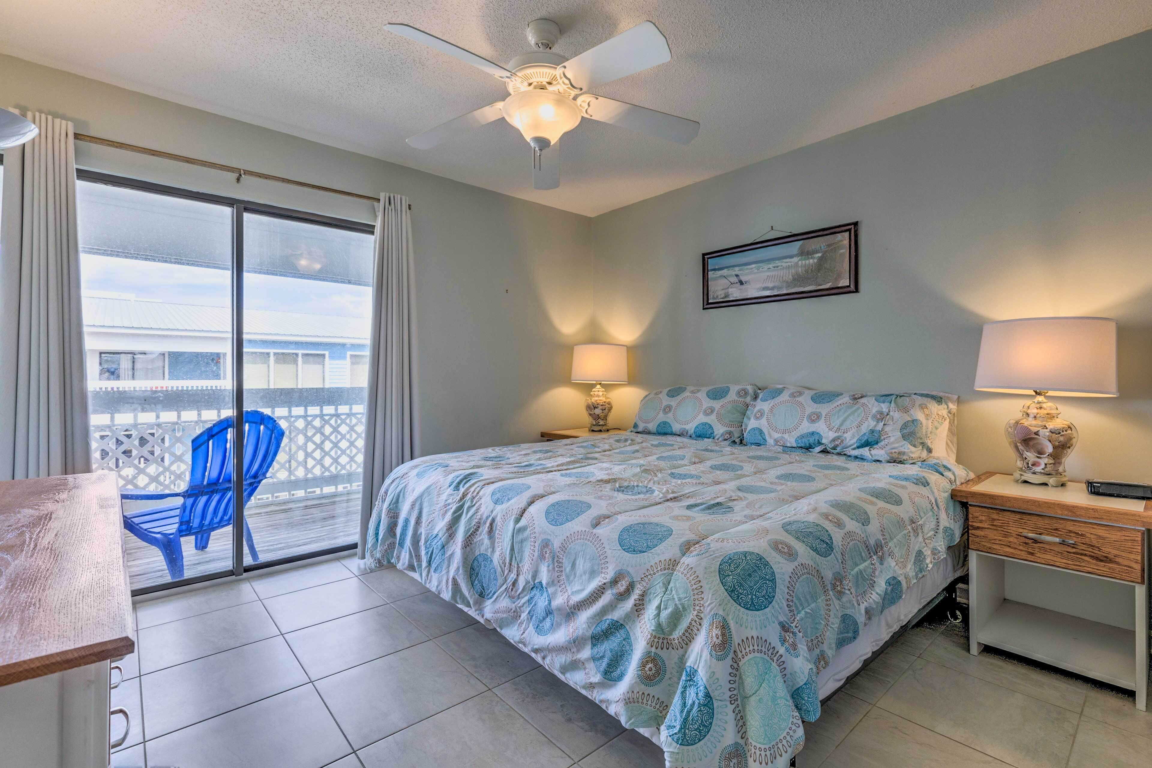 A bedroom with a bed, two bedside lamps, a ceiling fan, a desk, and a chair.