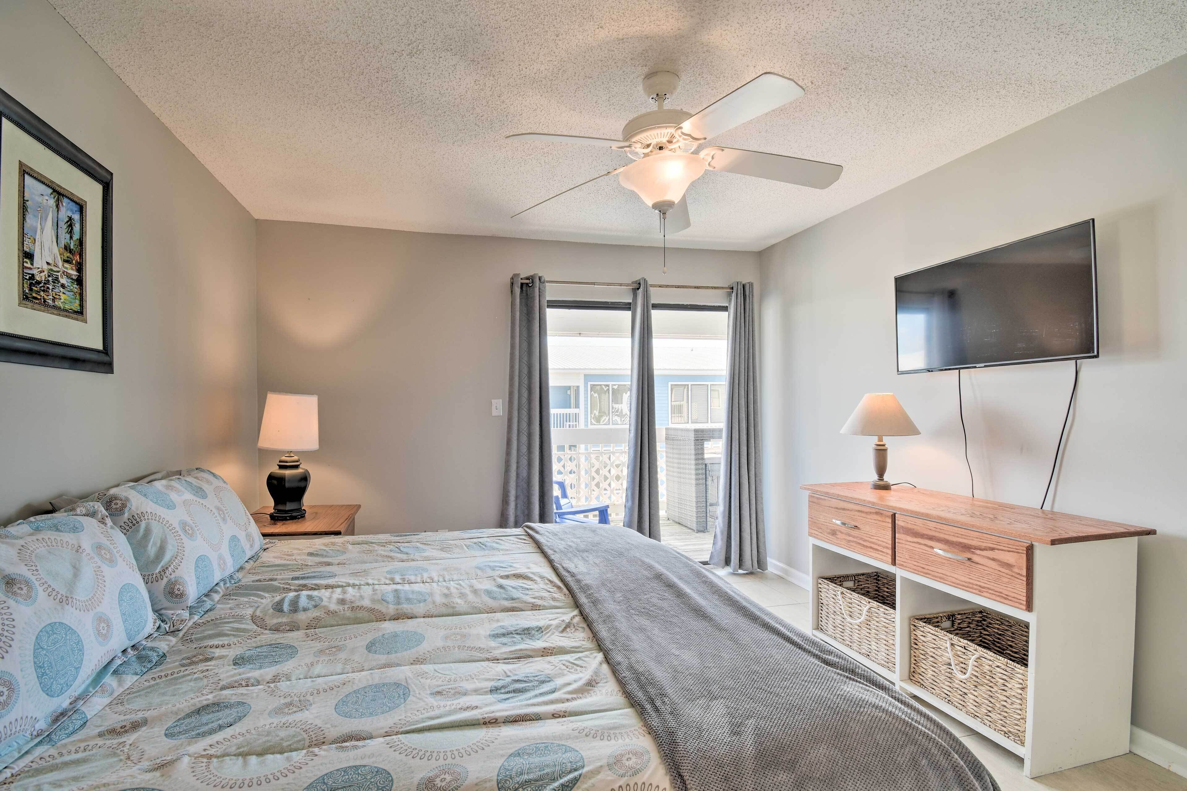 A bedroom with a bed, a ceiling fan, a TV, a nightstand, and a view of the outside balcony.