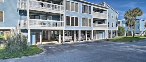 A multi-story hotel with balconies, a parking area, and a well-maintained lawn.