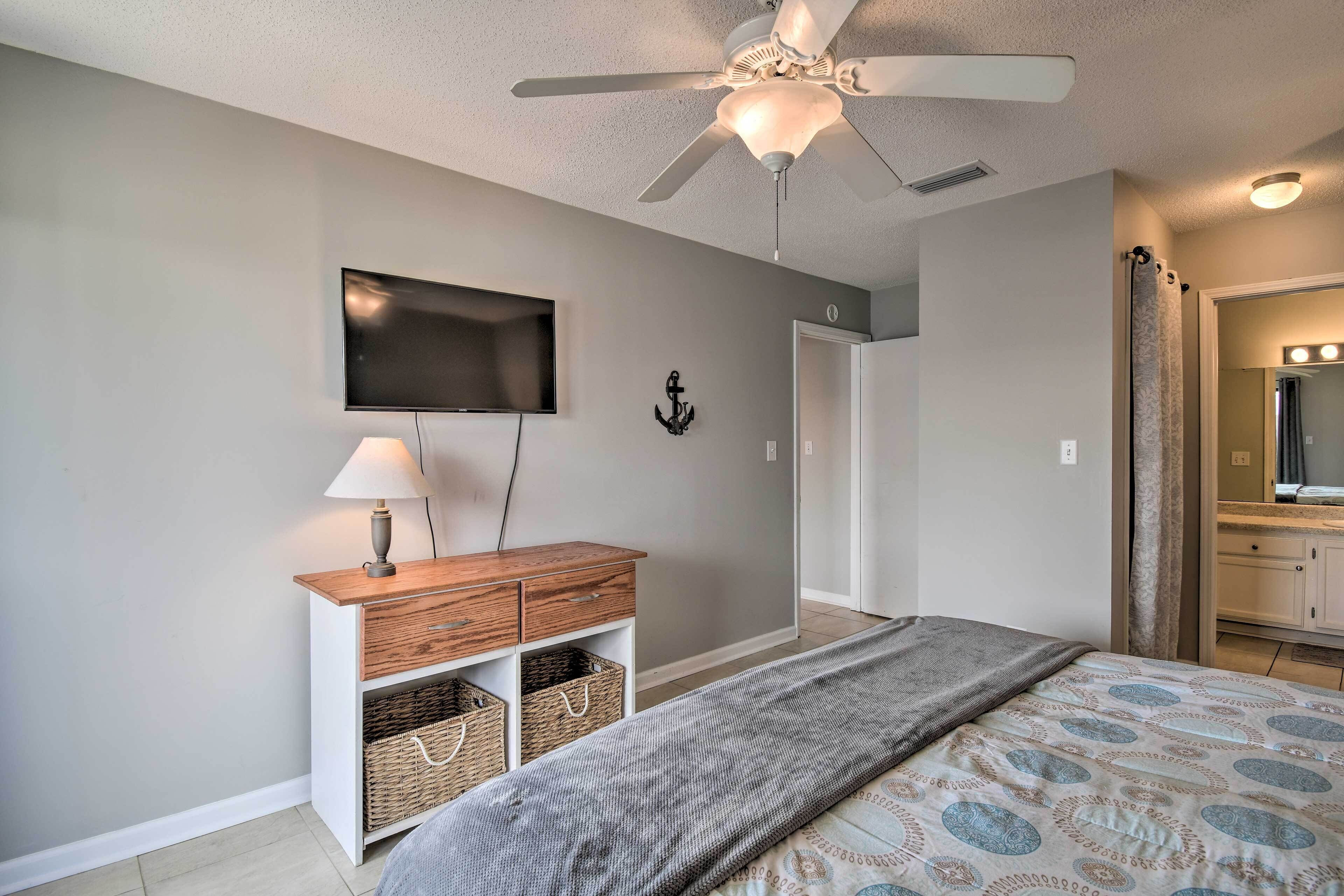 A bedroom with a bed, a ceiling fan, a TV, a dresser, and a bathroom with a mirror and curtains.