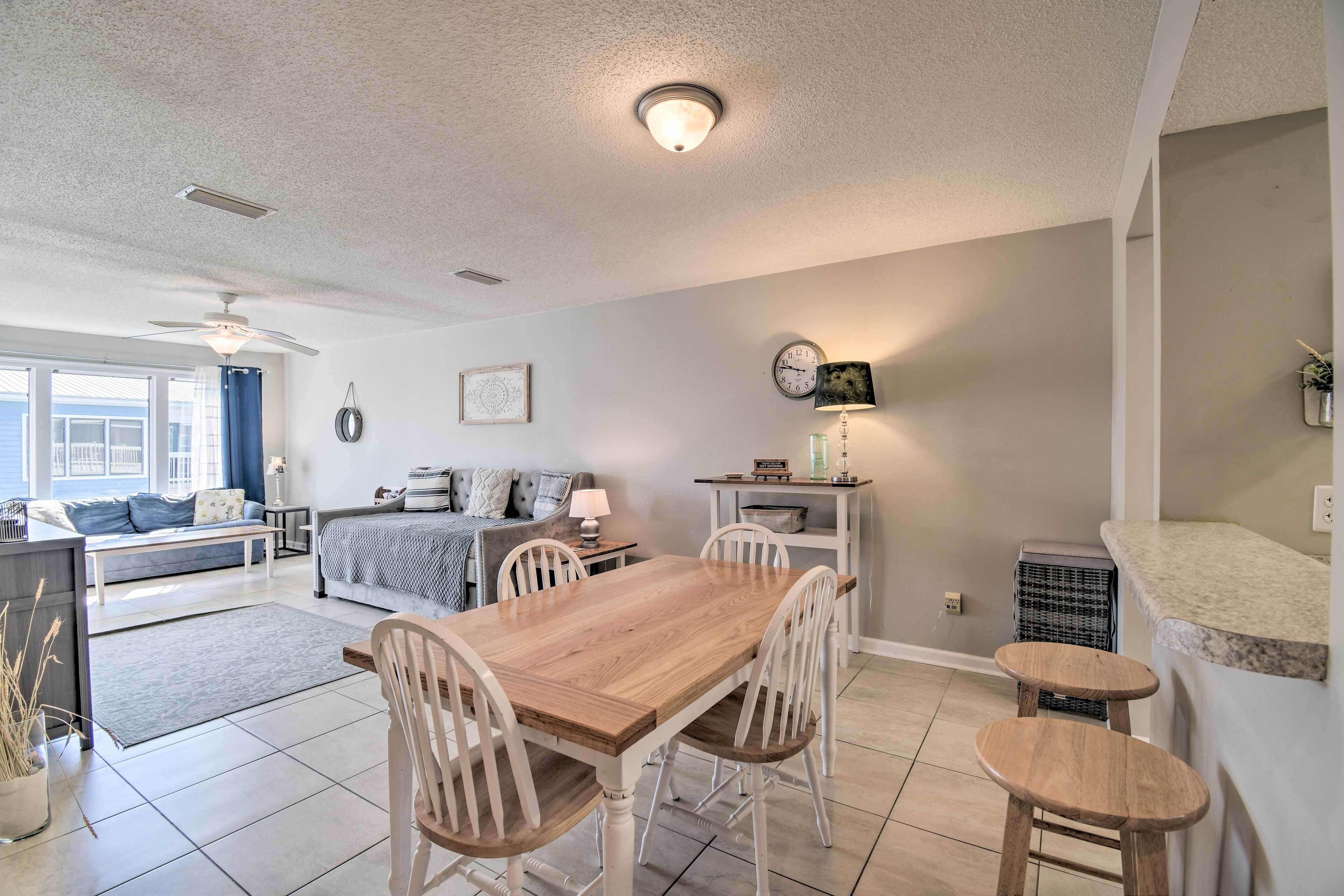 A modern kitchen with a wooden table and chairs, a dining area, and a living room with a sofa and a lamp.