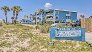Un immeuble d’appartements situé en bord de mer, avec une enseigne indiquant : « 1872 West Beach SeaOats Condominium ».