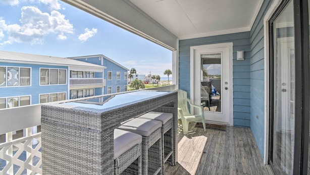 Un balcon agrémenté de meubles en osier, une vue sur un immeuble bleu et une porte donnant sur l’intérieur.