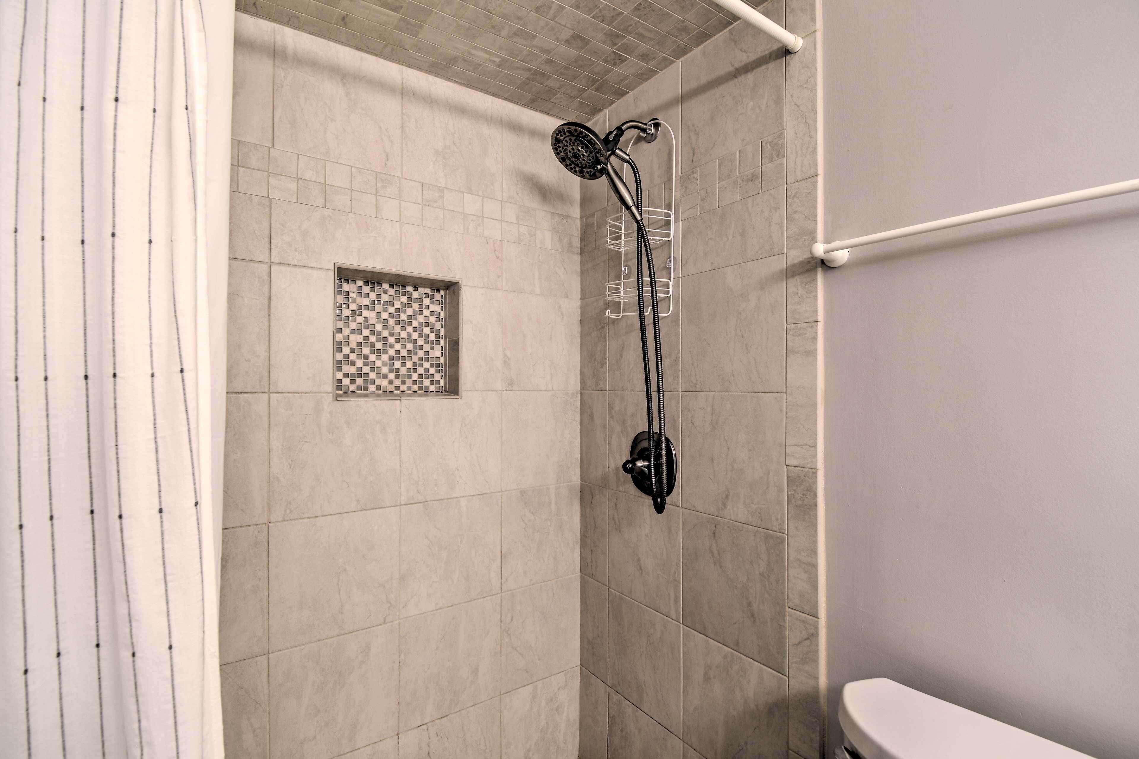 Et bruseområde med flisebeklædt væg, brusehoved og et hvidt toilet.