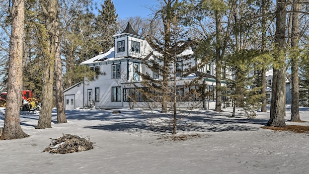 Een groot, wit, twee verdiepingen tellend huis met een opvallende toren, omgeven door hoge dennenbomen en een met sneeuw bedekte grond.
