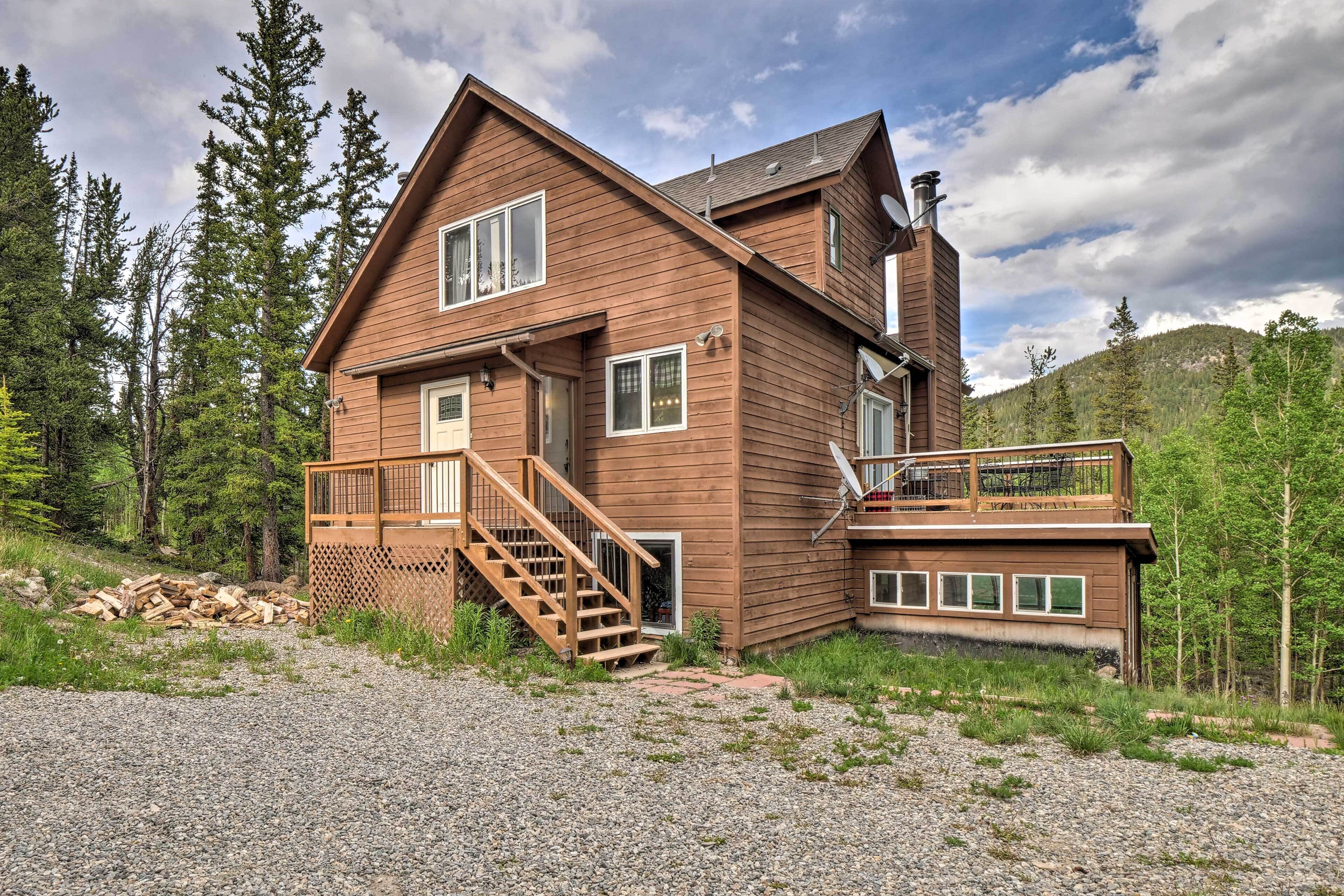 A two-story wooden cabin with a balcony, a staircase, and a view of the surrounding forest.