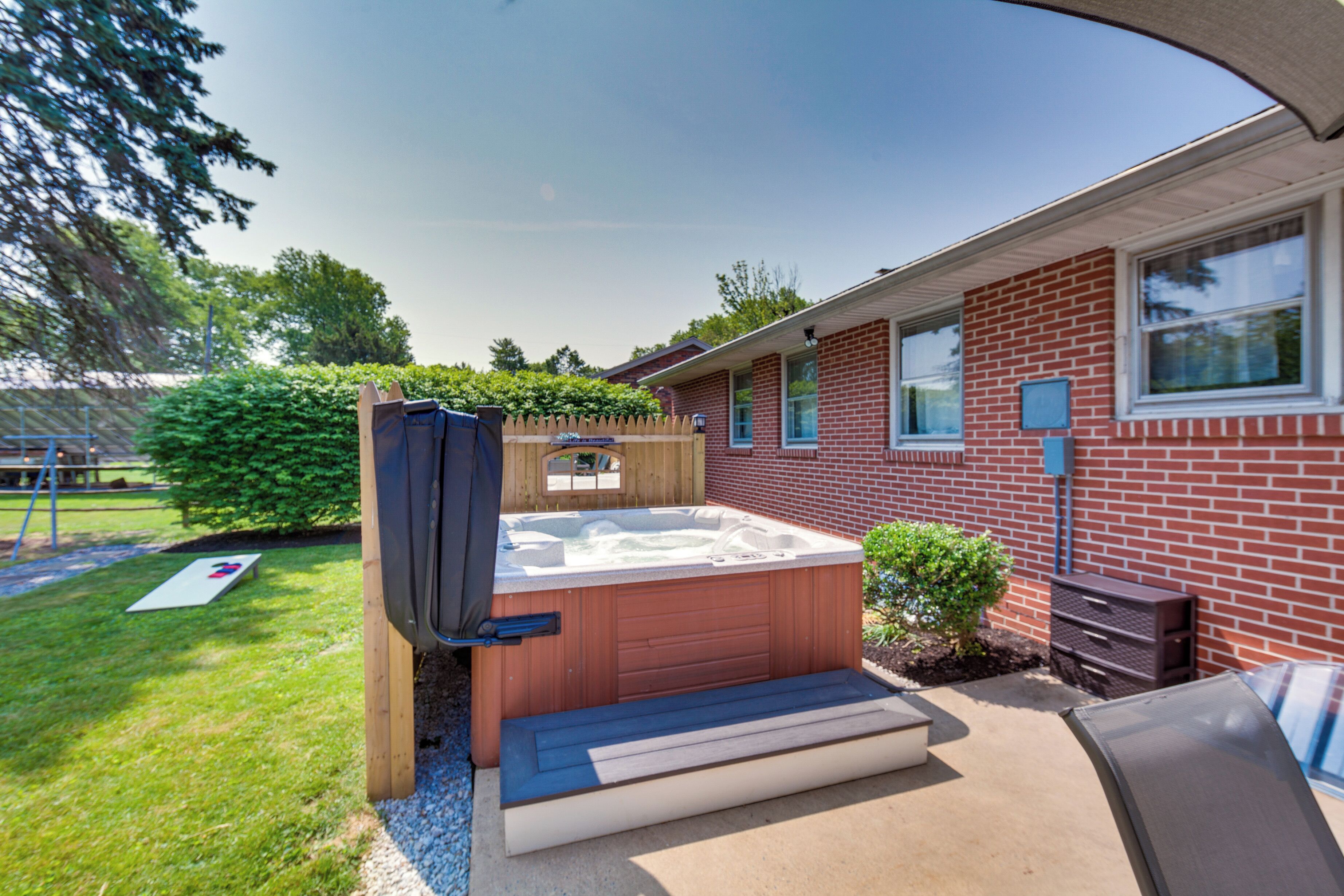 A backyard with a hot tub, a wooden deck, and a brick house.