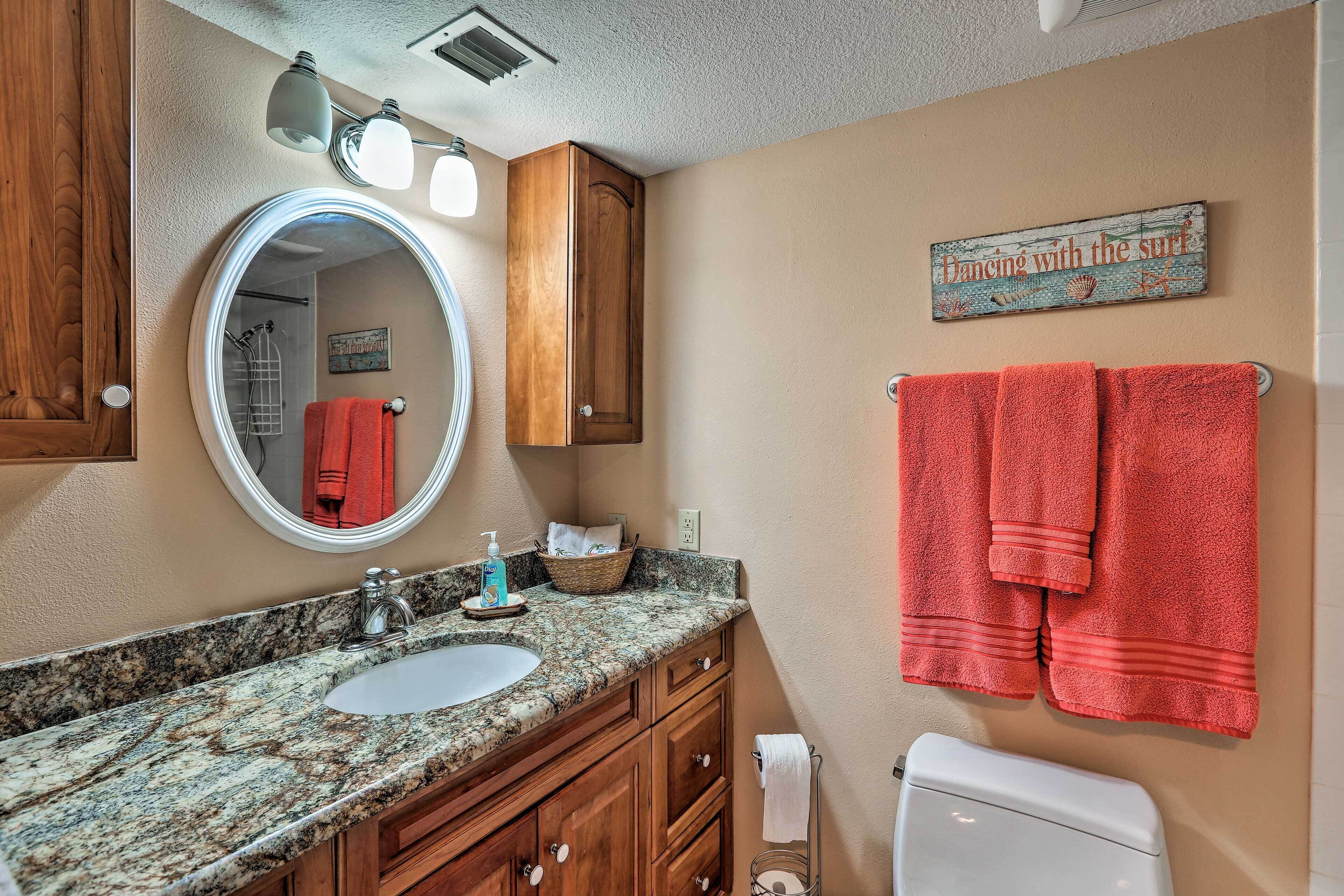 A bathroom with a granite countertop sink, wooden cabinets, a round mirror, and a towel rack with two red towels.