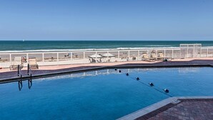 A swimming pool with a view of the ocean, a fenced deck area with lounge chairs, and a lifeguard stand.