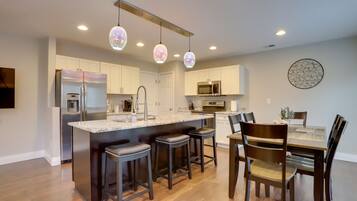 A modern kitchen with a central island, bar stools, a dining table with chairs, and pendant lighting.