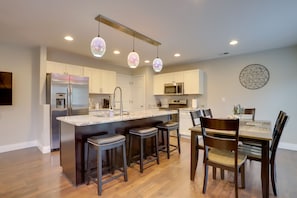 A modern kitchen with a central island, bar stools, a dining table with chairs, and pendant lighting.