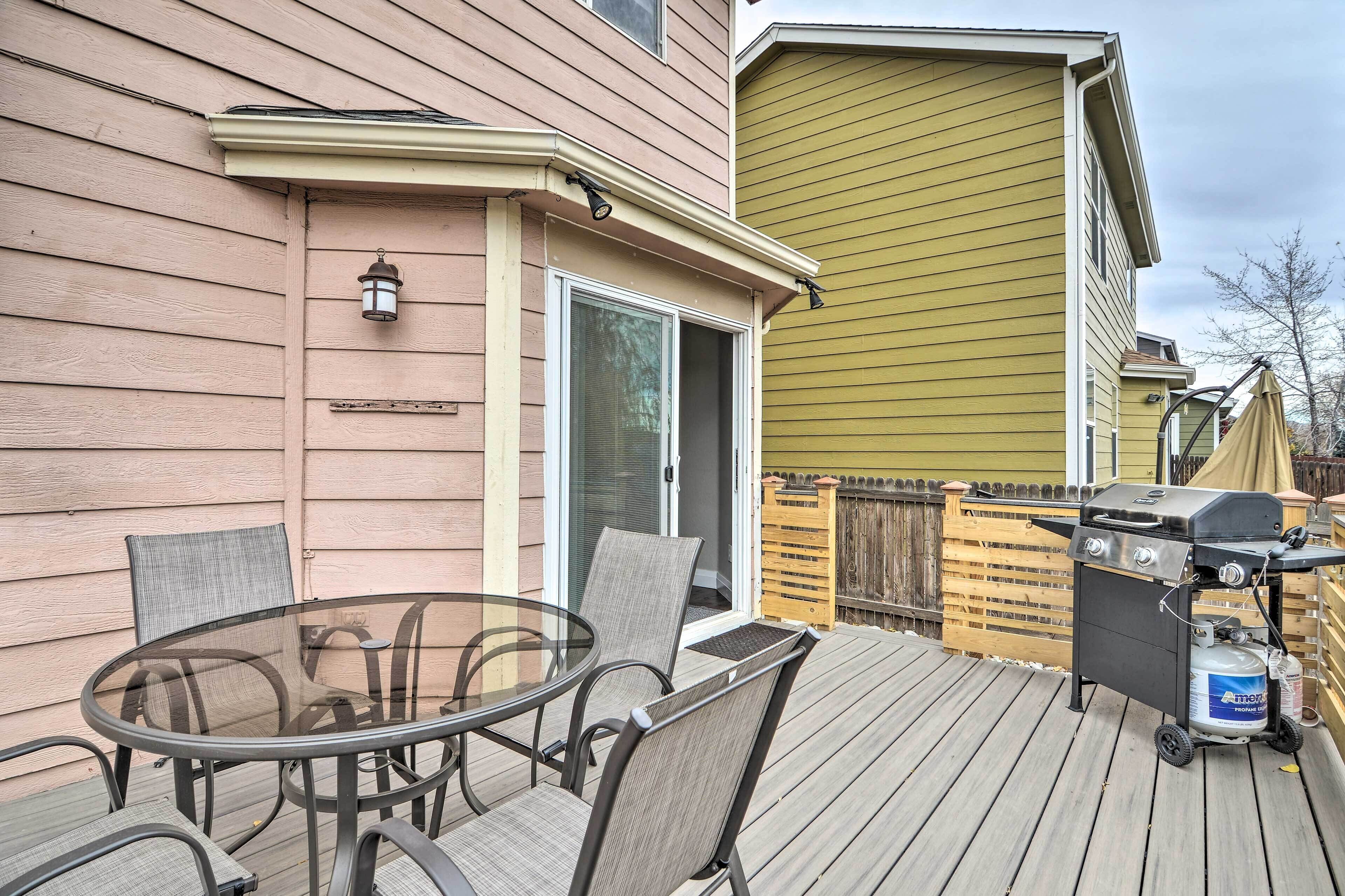 A deck with a glass-top table and chairs, a grill, and a sliding glass door.