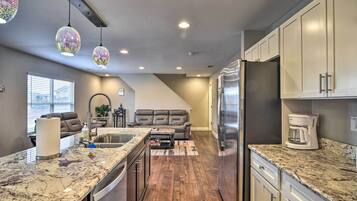 A modern kitchen with granite countertops, a refrigerator, and a coffee maker.
