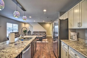 A modern kitchen with granite countertops, a refrigerator, and a coffee maker.