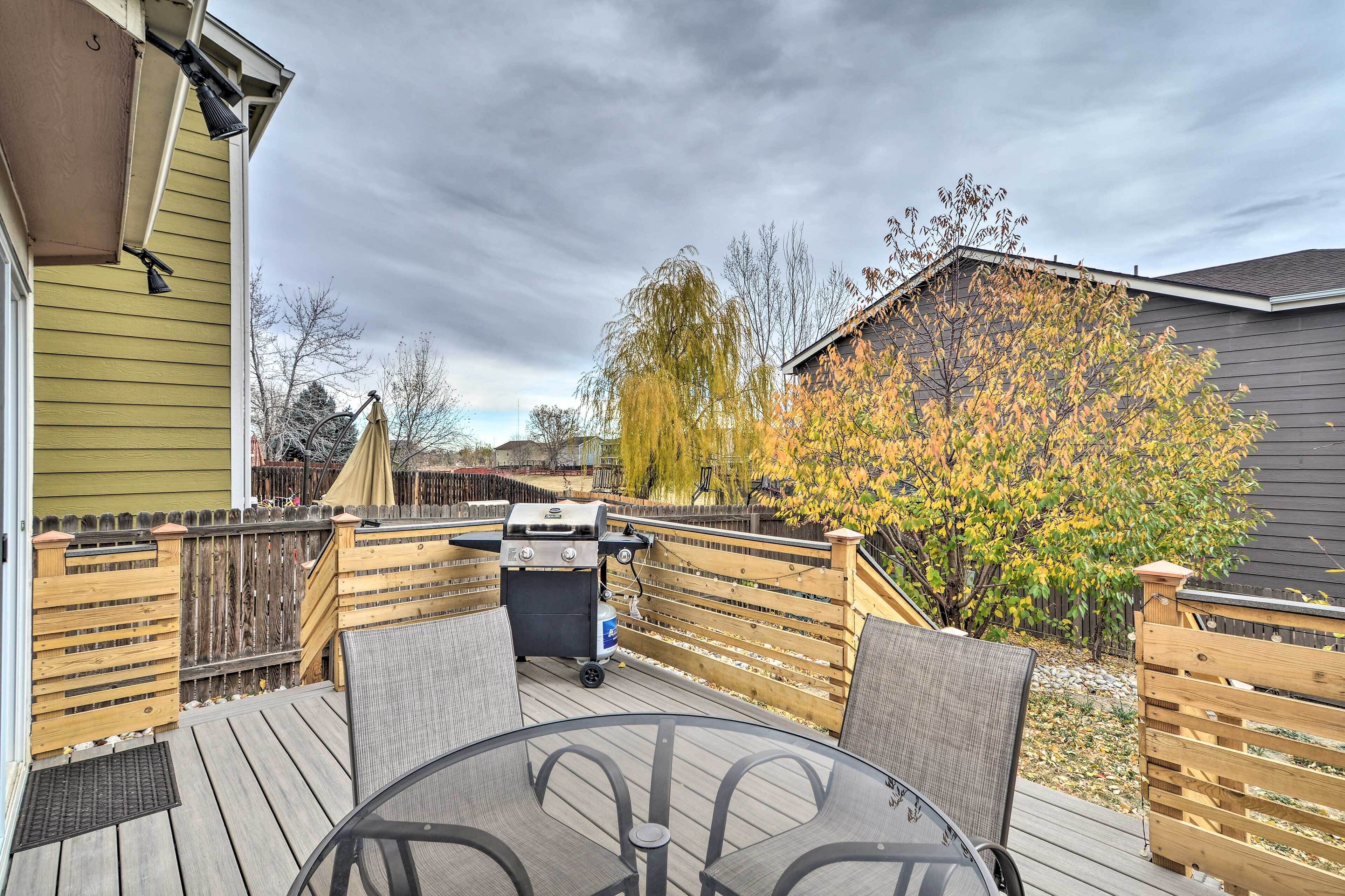 A deck with a grill, outdoor seating, and a wooden fence.