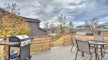 A wooden deck with a grill and a table with chairs, surrounded by a wooden fence and trees.