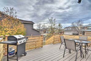 A wooden deck with a grill and a table with chairs, surrounded by a wooden fence and trees.