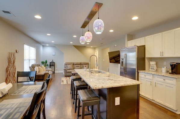 A modern kitchen with a large island, white cabinets, stainless steel appliances, and pendant lighting.