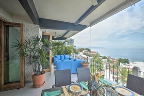 A balcony with a blue sofa, potted plants, and a dining table set. - Puerto Vallarta Condo w/ Pool - Walk to La Playa! (Puerto Vallarta)