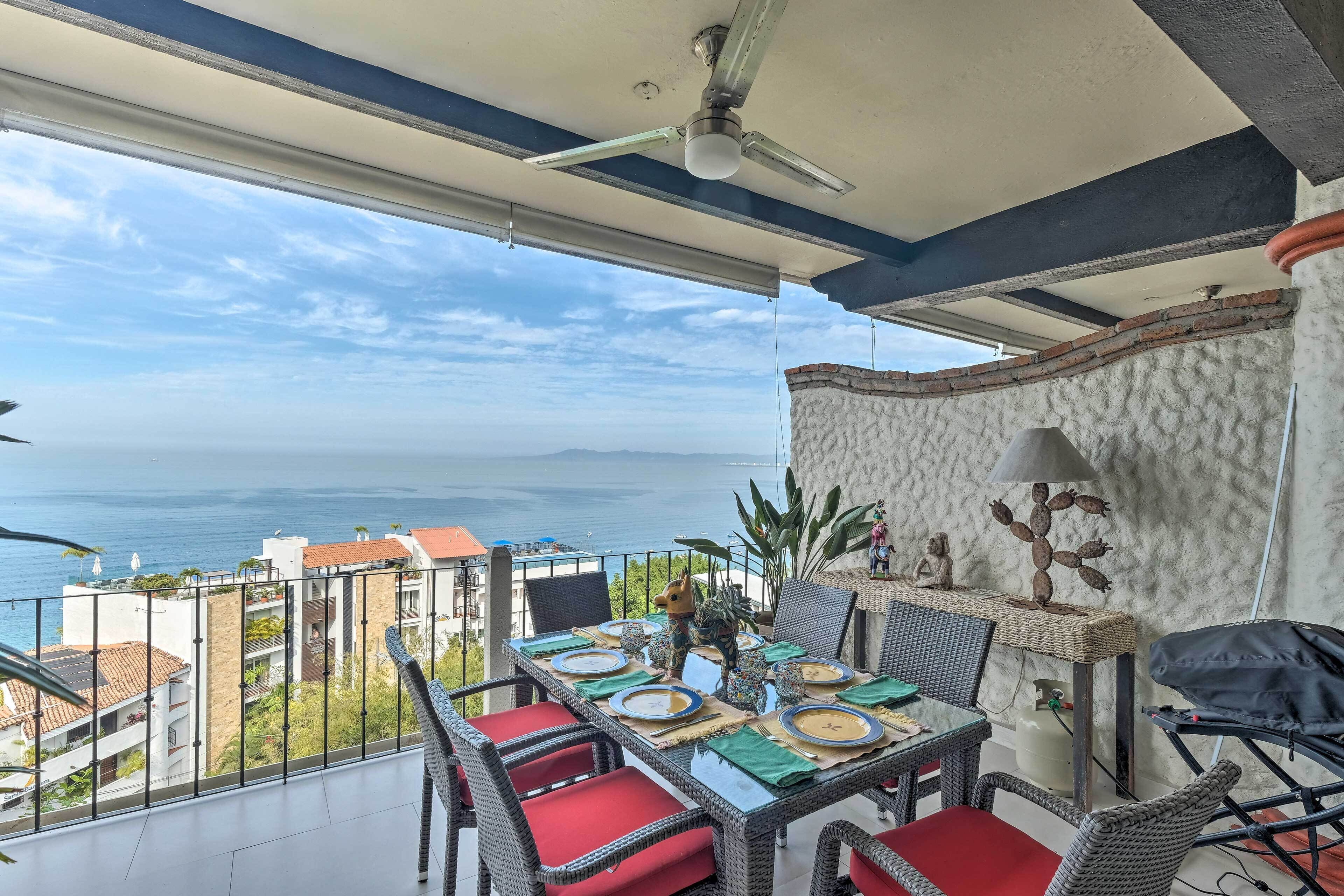 A balcony with a dining table set for four, overlooking a coastal view.