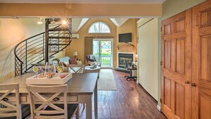 A dining area with a wooden table and chairs, a staircase, a fireplace, and a large wooden door. - Townhome w/ Fireplace - Walk to Chairlift! (Ellicottville)