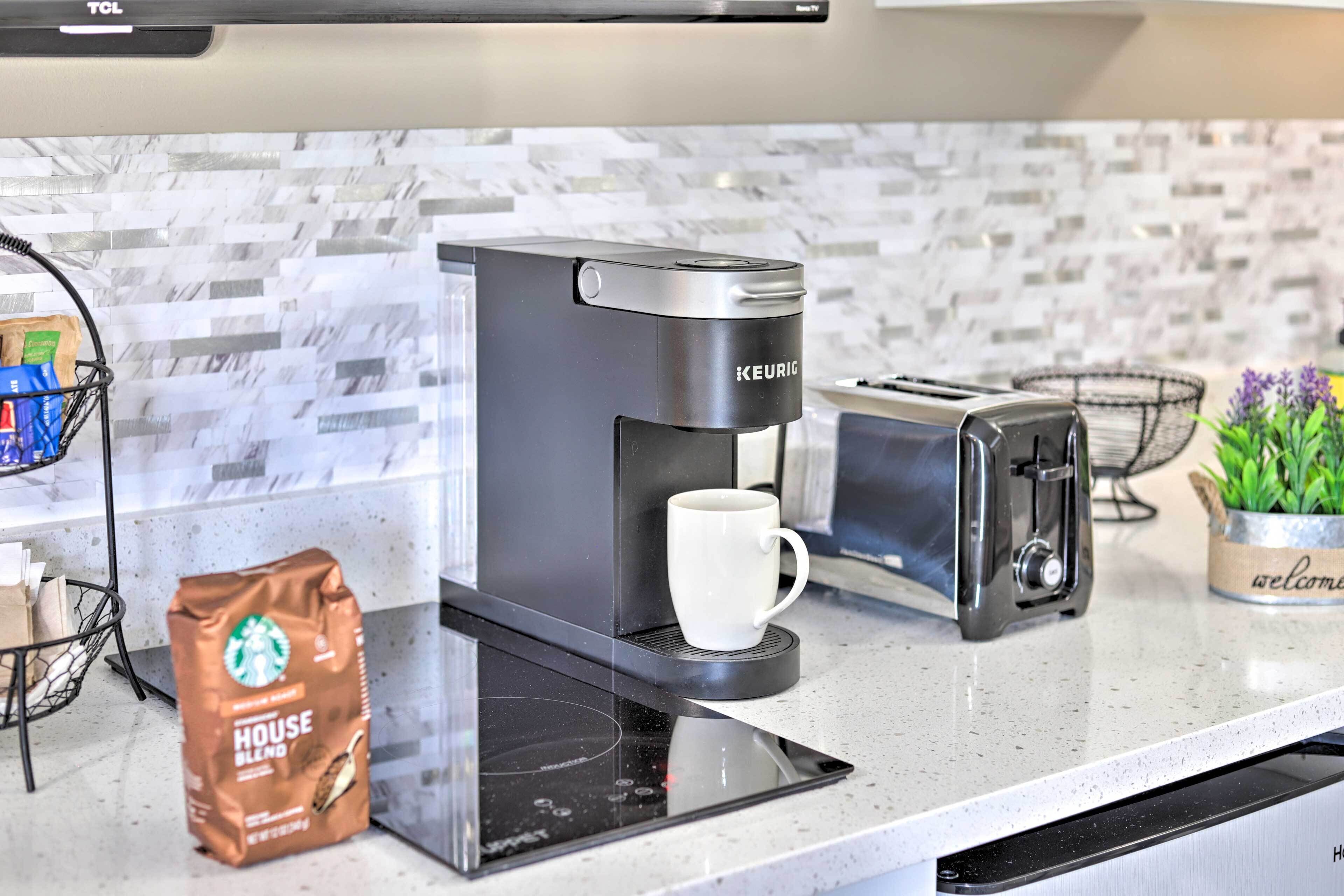Een Keurig koffiezetapparaat op een keukentafel met een witte mok, een broodrooster en een zak koffie van Starbucks.