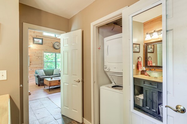 A hallway with a door leading to a laundry room and a living area with a sofa and a clock. - Hillside Cabin on 43 Acres w/ Private Lake & View! (Defiance)
