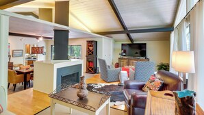 Een ruime woonkamer met een open haard, comfortabele zithoek en een moderne keuken op de achtergrond.