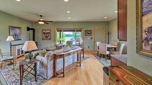 A spacious living room with a sofa, coffee table, and dining area. There are ceiling lights, a ceiling fan, and a large window providing natural light. - Cabin w/ Porch & View ~ 19 Mi to West Glacier (Columbia Falls)