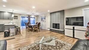 A modern living room with a glass coffee table, a fireplace, a TV, and a dining area with wooden chairs. - Spacious Kent Home ~ 17 Mi to Dtwn Seattle! (Kent)