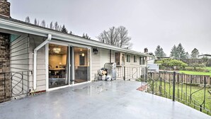 A covered patio with a concrete floor, a sliding glass door leading to a kitchen, and a small outdoor grill area. - Spacious Kent Home ~ 17 Mi to Dtwn Seattle! (Kent)