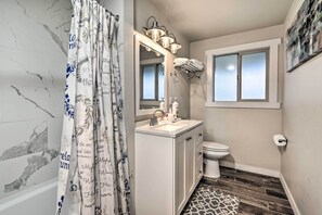 Ein Badezimmer mit Duschvorhang mit inspirierenden Sprüchen, einem Schminktisch mit Spiegel und Beleuchtung, einer Toilette und einem Fenster mit blickdichter Verglasung.