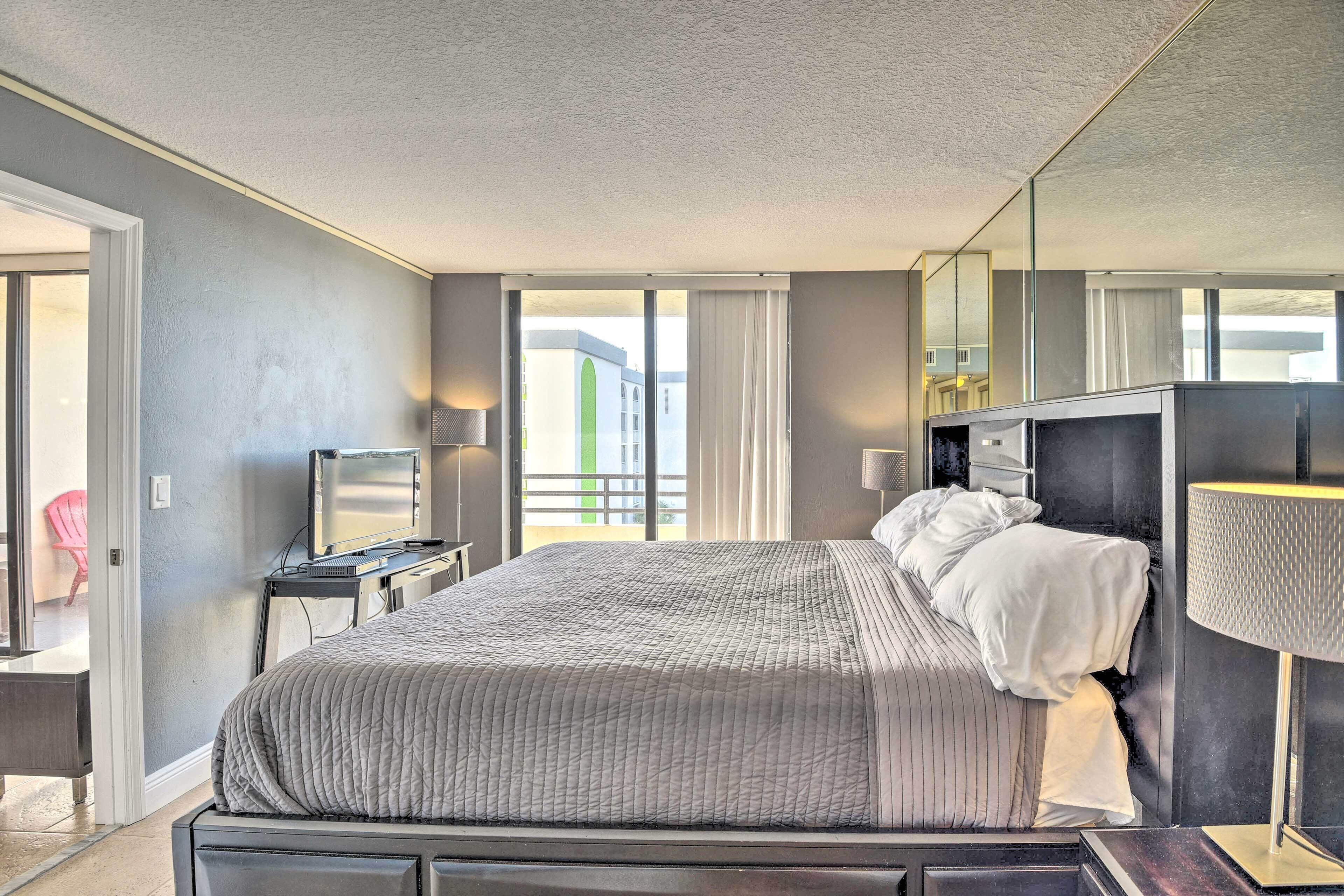 Habitación de hotel moderna con una cama grande, un escritorio, un televisor y vistas al balcón.