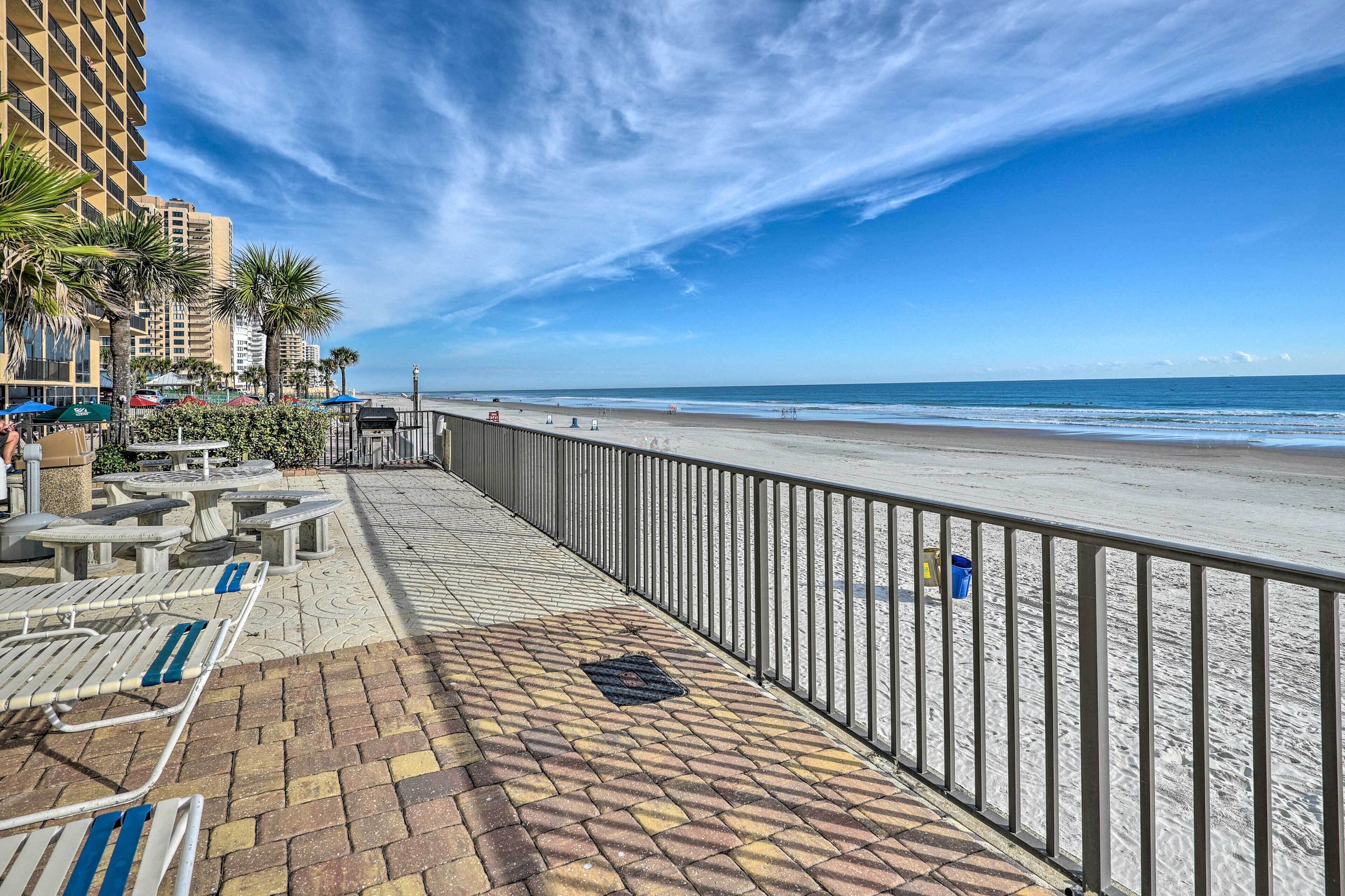 A beachside walkway with a railing, benches, and palm trees.