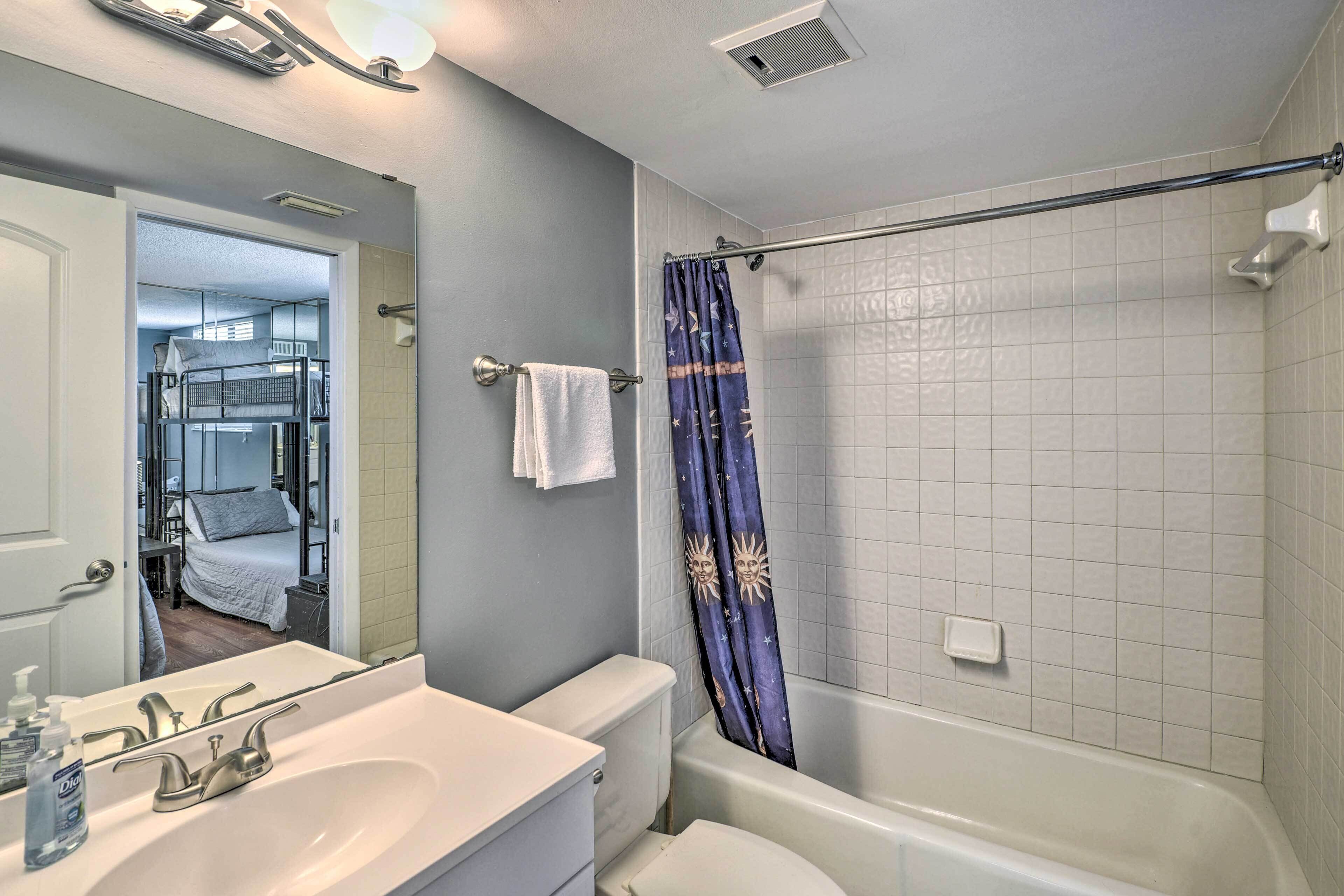 A bathroom with a white sink, mirror, and toilet. There is a shower curtain with a sun design, and a towel hanging on the wall.