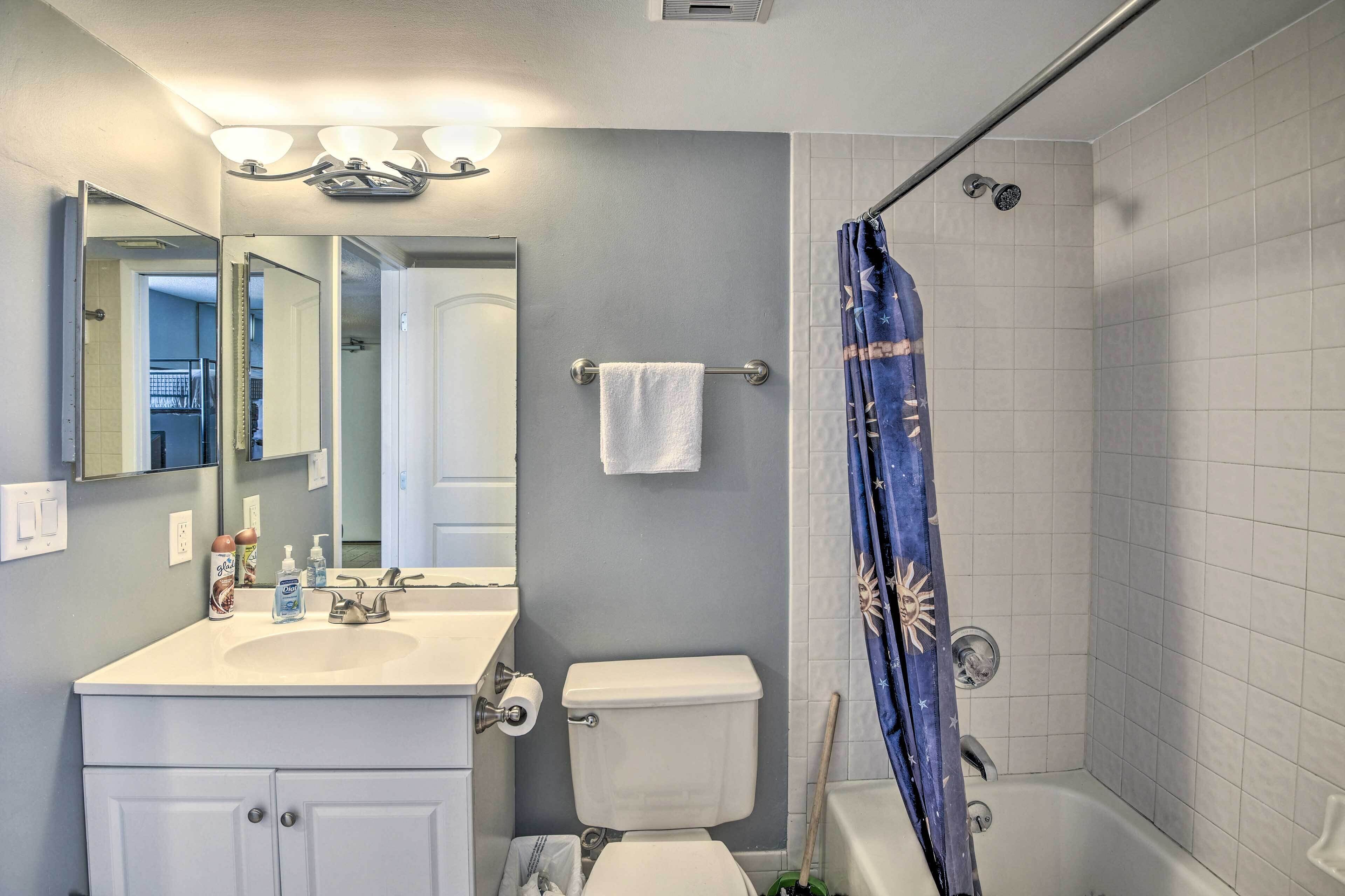 A bathroom with a white sink, mirror, and toilet. There is a shower curtain with a sun design.