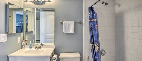 A bathroom with a white sink, mirror, and toilet. There is a shower curtain with a sun design.