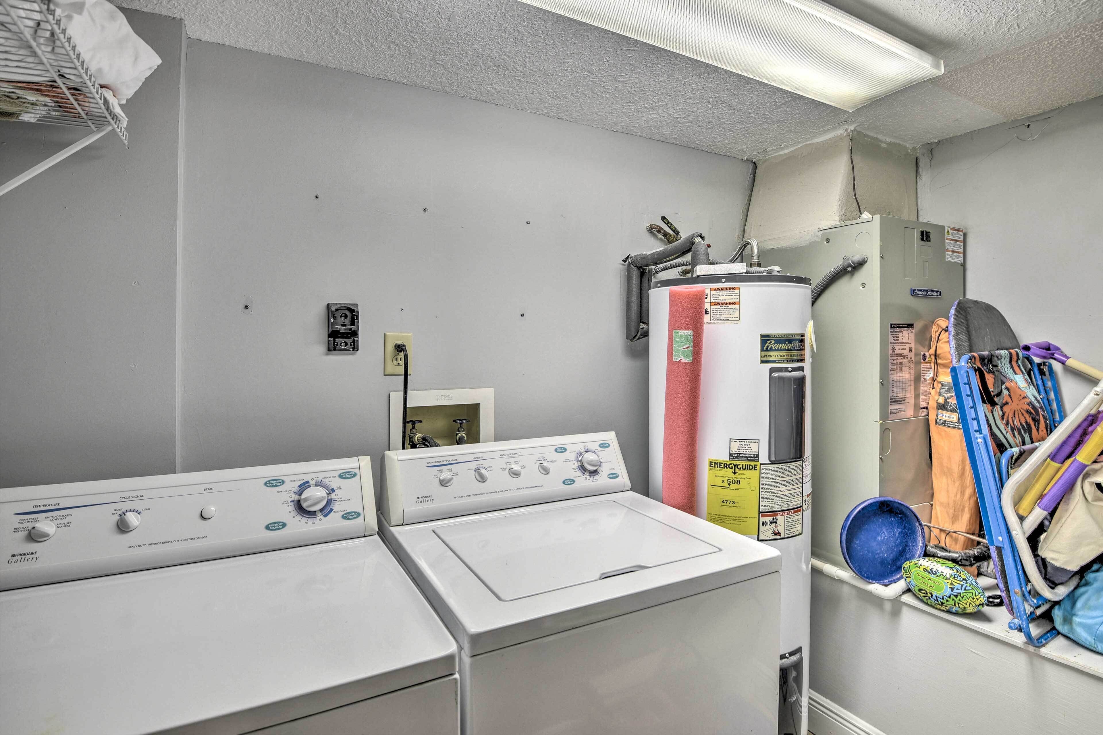 Une buanderie équipée de deux machines à laver et deux sèche-linge, d’un chauffe-eau et d’une étagère où sont rangés les produits de nettoyage.